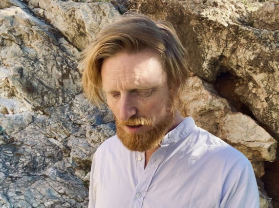 Image shows Ryan Board filming outdoors near a rocky outcrop in Athens, 2025